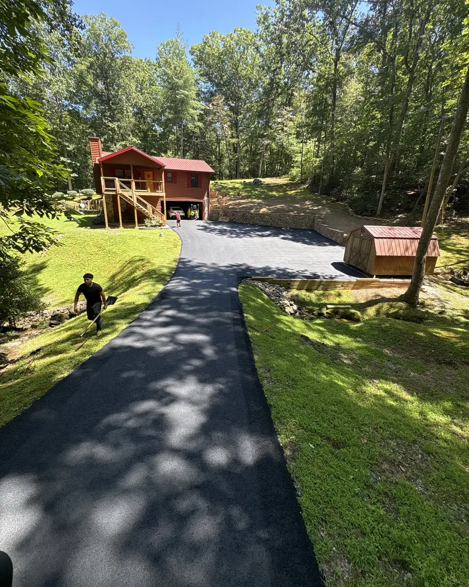 New asphalt driveway climbing a wooded hillside to a red-roofed cabin