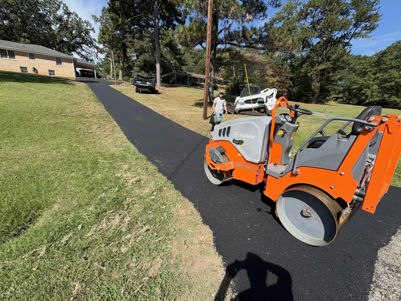 HAMM roller compacting a fresh asphalt driveway between residential homes
